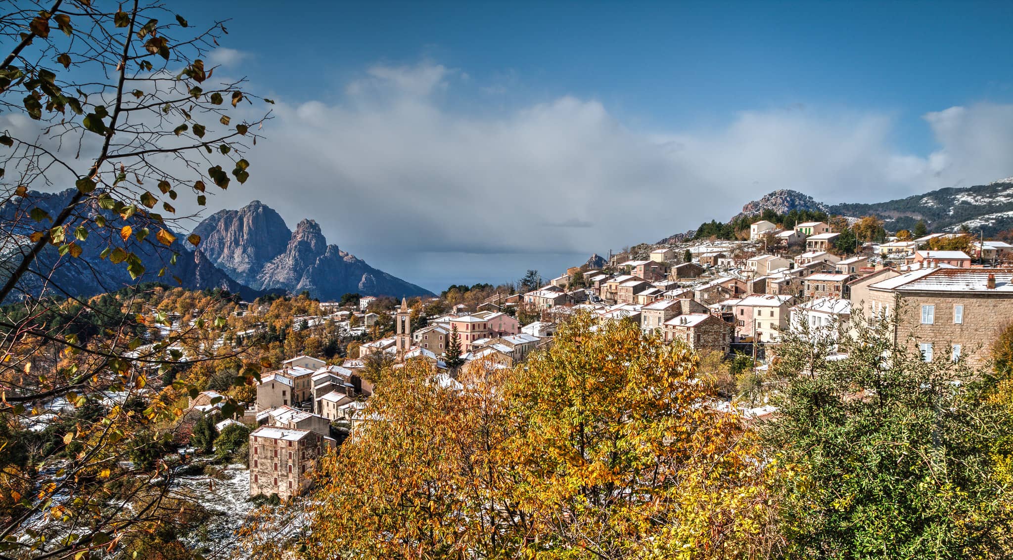 Paysage d'Evisa en Corse. Feuillages, maisons et montagnes au loin.