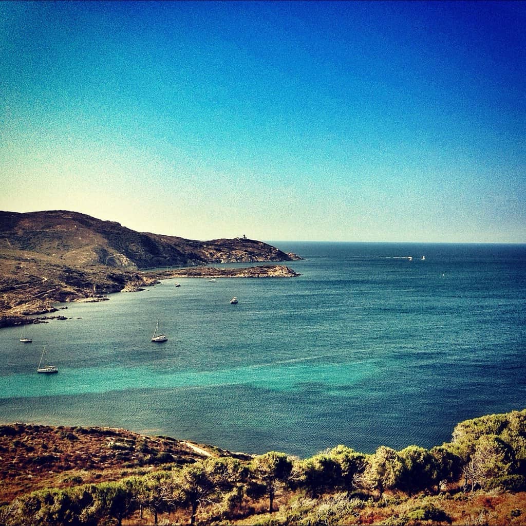 Panorama de la presqu’île de la Revellata. Mer bleu turquoise ou voguent des bateaux faisant face à la terre couverte de végétation. Phare de la Revellata à l'arrière-plan.